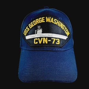 May include: Navy blue baseball cap featuring a patch with the text "USS GEORGE WASHINGTON" and "CVN-73". The patch includes an image of a ship in white and black. The cap is made of a durable fabric.