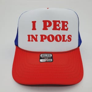 May include: A red, white, and blue trucker hat with the text "I PEE IN POOLS" in red block letters. The hat has a white front panel, a red brim, and a blue mesh back. The hat has a "OTTO" brand tag.