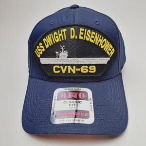 May include: Navy blue baseball cap featuring a patch with the text "USS DWIGHT D. EISENHOWER" and "CVN-69". The cap has a curved brim and a tag that reads "OTTO CLASSIC FIT".