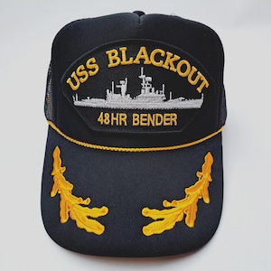 May include: Black trucker hat with a mesh back and a curved brim. The front patch features the text "USS BLACKOUT" above a ship illustration and "48HR BENDER". Gold leaf embroidery accents the brim.