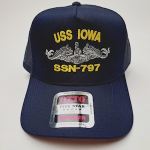 May include: Navy blue trucker hat with the text "USS IOWA" and "SSN-797" embroidered in yellow. The hat features a mesh back and a snap closure. A white and red label is visible on the front.