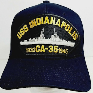 May include: Navy blue baseball cap featuring a patch with the text "USS INDIANAPOLIS" in gold lettering. The patch also includes a ship illustration and the dates "1932 CA-35 1945". The cap has a curved brim and a button on top.
