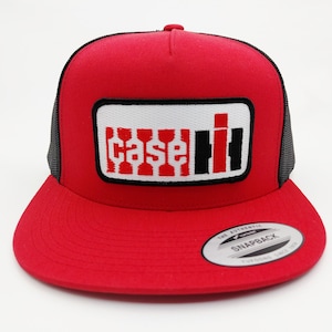 May include: A red snapback hat with a black mesh back and a flat brim. The front features a white rectangle with the words "case ih" in red and black. The hat has a snap closure and a small white tag on the brim.
