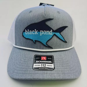 May include: Gray trucker hat with a white mesh back and a black and blue fish logo. The text "black pond" is embroidered on the front. The hat has a white rope detail and an adjustable strap.
