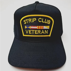 May include: Black baseball cap with a flat brim. The cap features a yellow and black patch with the words "STRIP CLUB VETERAN" and a colorful emblem.