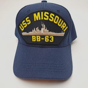 May include: Navy blue baseball cap featuring a patch with the text "USS MISSOURI" in yellow, along with a ship illustration and "BB-63". The cap has a curved brim and a button on top. A classic, casual accessory.