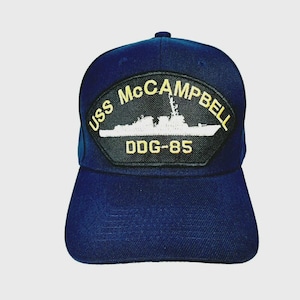 May include: A navy blue baseball cap featuring a patch with the text "USS McCampbell DDG-85" in gold and white. The patch displays a white illustration of a ship. The cap is made of a durable fabric and has a curved brim.