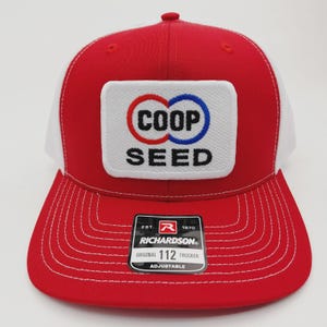 May include: Red and white trucker hat with the text "COOP SEED" on a white patch. The hat has a red brim and crown, a white mesh back, and an adjustable strap. The Richardson brand label is visible.