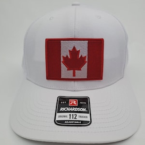 May include: White trucker hat with a red and white Canadian flag patch. The hat features a curved brim and an adjustable snapback closure. The Richardson brand label is visible on the front.