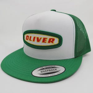 May include: A white and green snapback trucker hat with the name "OLIVER" in a yellow and red font on a green patch. The hat has a green brim and mesh back, with a "Yupoong" tag.