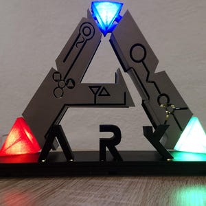 May include: An illuminated ARK logo in black and grey, with a blue diamond at the top and red and green triangles at the base. The letters "ARK" are visible. The design incorporates circuit-like patterns and geometric shapes.
