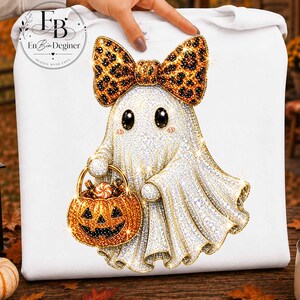 Può includere: Una felpa bianca con la grafica di un fantasma ricoperto di strass scintillanti. Il fantasma indossa un grande fiocco con stampa leopardata e tiene in mano un secchiello arancione a forma di zucca per dolci. Il design ha un effetto glitterato.