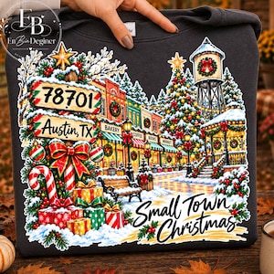 May include: A dark gray sweatshirt featuring a colorful graphic of a snowy town square at Christmas. The design includes a street sign reading 78701 Austin, TX, a decorated tree, a water tower, gift boxes, and the text Small Town Christmas.