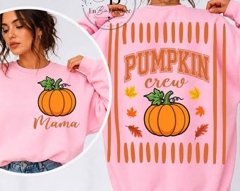 May include: A light pink long-sleeve sweatshirt featuring a graphic of an orange pumpkin with green leaves. The front displays the word Mama, while the back features the text Pumpkin crew with a larger pumpkin graphic and scattered autumn leaves.