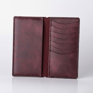 May include: Open burgundy leather wallet with multiple card slots and a large pocket. The wallet is stitched with a contrasting thread and has a smooth, polished finish. The interior is a darker shade of burgundy.