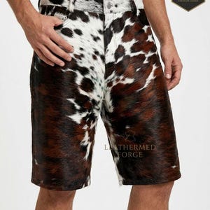 May include: Cowhide shorts with a brown, white, and black spotted pattern. The shorts have a classic five-pocket design with a button and zipper closure. The shorts are made of a soft, textured material.