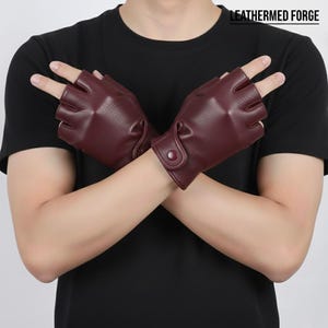 Puede incluir: Guantes de cuero burdeos sin dedos con cierre de botón. El texto "LEATHERMED FORGE" es visible en la esquina superior derecha. Los guantes son de color rojo intenso y parecen estar hechos de cuero suave.