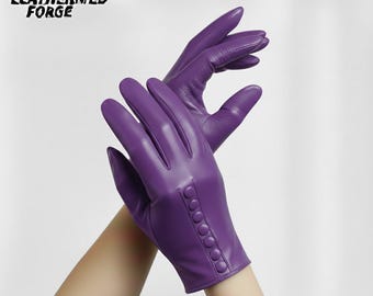 May include: A pair of vibrant purple leather gloves. The gloves have a smooth texture and are adorned with a row of small, matching buttons on the wrist. The brand name "LEATHERMED FORGE" is visible in the upper left corner.