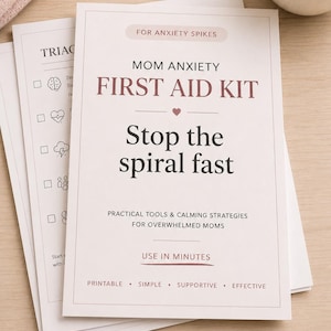 May include: Printed papers with the text "MOM ANXIETY FIRST AID KIT" in maroon. The text "Stop the spiral fast" is below. The papers also include the text "FOR ANXIETY SPIKES" and "PRACTICAL TOOLS & CALMING STRATEGIES FOR OVERWHELMED MOMS".