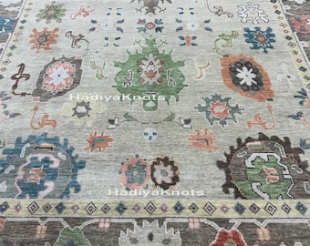 May include: A large, rectangular area rug with a beige background and intricate, colorful floral and geometric patterns. The rug features a dark brown border and the text "HadiyaKnots".