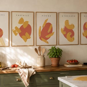 K&ouml;nnte beinhalten: F&uuml;nf gerahmte Wandbilder mit Illustrationen von Nudelsorten, beschriftet mit Spaghetti, Farfalle, Penne, Hornchen und Rigatoni. Jeder Druck zeigt gelbe Nudeln &uuml;ber einer roten Kreisform auf cremefarbenem Grund in hellen Holzrahmen.
