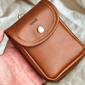 May include: A white ceramic mug with a black handle and the text "But First, Coffee" in a bold, black font. The mug is set against a blurred background, suggesting a cozy setting.