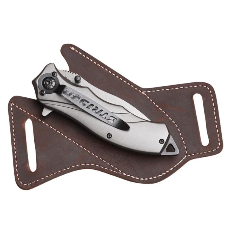 Peut inclure: Un couteau pliant argent&eacute; avec le mot "STRIDER" sur le clip, pos&eacute; dans un &eacute;tui en cuir marron. L'&eacute;tui a des coutures blanches et deux passants de ceinture. Le couteau est un outil tactique.