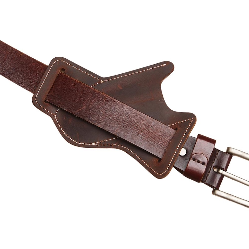 Peut inclure: Gros plan sur une ceinture en cuir marron avec un motif en forme de guitare. La ceinture comporte une sangle rectangulaire et une boucle argent&eacute;e. Des coutures blanches soulignent la forme de la guitare.