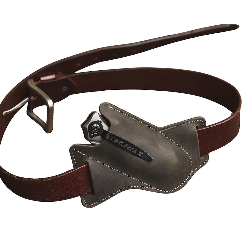 Peut inclure: Une ceinture en cuir marron avec une boucle argent&eacute;e et un &eacute;tui en cuir gris contenant un couteau pliant. Le couteau a un manche noir et le mot "STRIDER" est imprim&eacute; sur la lame.