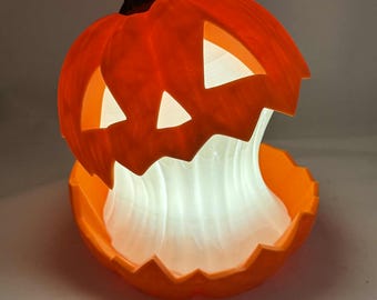 May include: An illuminated orange pumpkin decoration with a carved face. The pumpkin is split open, revealing a glowing white interior. A black stem sits atop the pumpkin. The decoration is likely for Halloween.
