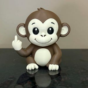 May include: A brown and white figurine of a cartoon monkey sitting down, giving the middle finger. The monkey has large black eyes, a white belly, and white hands and feet. The figurine is on a reflective surface.
