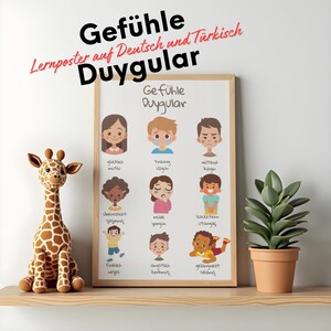 Puede incluir: Un póster enmarcado con las palabras "Gefühle Duygular" e ilustraciones de diferentes emociones. Una jirafa de peluche y una planta en maceta están en una estantería de madera.
