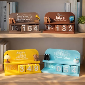 May include: Four decorative wooden book reading counters in brown, yellow, and blue. Each counter has a shelf with books and a number display. The brown counters read "Books Read This Year" and "Jake's Reading This Year". The yellow counter reads "Ruby's Completed Reads". The blue counter reads "Hannah's Library".
