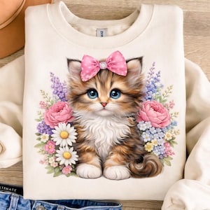 May include: Cream-colored sweatshirt featuring a watercolor illustration of a kitten with blue eyes and a pink bow. The kitten is surrounded by pink roses, daisies, and lavender flowers. A cute and adorable design.