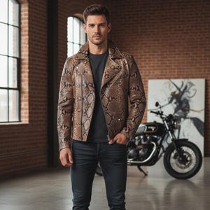 Puede incluir: Chaqueta de cuero marrón y beige con estampado de piel de serpiente y cierre de cremallera negro. La chaqueta tiene un estilo motero clásico con cuello de solapa y silueta entallada. El modelo lleva una camiseta negra y vaqueros azul oscuro.