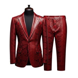 May include: A red snakeskin-effect suit, comprising a blazer and matching trousers, presented on a mannequin. The blazer features a notched lapel, two front pockets, and a single-button fastening. The trousers have a standard fit. The suit is made of a glossy material.