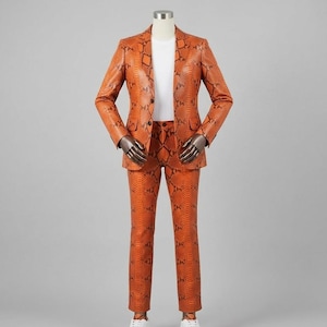 May include: A full-length shot of an orange snakeskin-patterned suit on a mannequin. The suit includes a blazer with a two-button closure and matching pants. The mannequin is wearing a white t-shirt underneath the blazer and white sneakers.