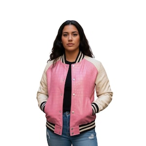 Puede incluir: Chaqueta universitaria rosa y crema con textura de cocodrilo sintético. La chaqueta tiene puños y dobladillo a rayas blancas y negras. La chaqueta está abotonada y tiene un forro negro.