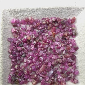 Peut inclure: Une collection de petites pierres précieuses rubis brutes et non polies dans des nuances variées de rose vif et de magenta profond. Les pierres sont de forme et de taille irrégulières, avec un mélange de textures translucides et opaques.