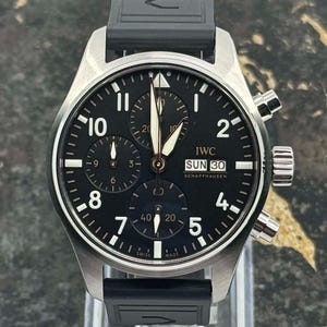 Peut inclure: Une montre IWC Schaffhausen en acier inoxydable avec un cadran noir et un bracelet en caoutchouc noir. Le cadran comporte des chiffres blancs, des sous-cadrans et le jour de la semaine. La montre a une fonction chronographe.