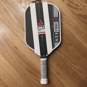 May include: A new Joola Pro Perseus pickleball paddle with a black and white striped design. The paddle has a white grip and the brand name is visible. The paddle is 16 mm thick and has a USA label.
