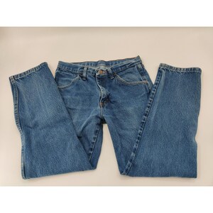 Puede incluir: Vaqueros de mezclilla azules con un diseño clásico de cinco bolsillos. Los vaqueros tienen cierre de botón y cremallera, trabillas para el cinturón y un corte de pierna recto. El denim tiene un lavado medio con algo de decoloración y desgaste.