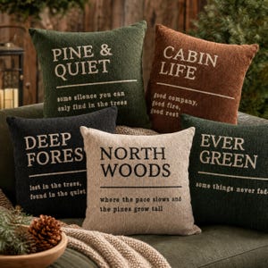 May include: Five square throw pillows with textured fabric. Colors include dark green, brown, charcoal, and beige. Each pillow features printed text such as PINE & QUIET, CABIN LIFE, DEEP FOREST, NORTH WOODS, and EVER GREEN, along with descriptive phrases.