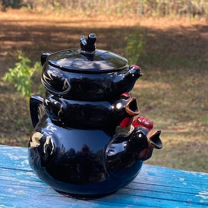 May include: A black ceramic stacking teapot set shaped like three chickens. The glossy black glaze features hand-painted white and gold accents on the wings. Each section includes a chicken head with a red comb and a beak that serves as a spout.