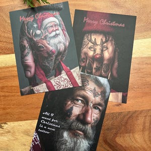 Op de afbeelding: Drie kerstkaarten met afbeeldingen van getatoeëerde handen en gezichten. Eén kaart toont de kerstman en een rendier, een andere een rendier met een rode neus en de derde een man met de tekst "All I want for Christmas is a new tattoo."