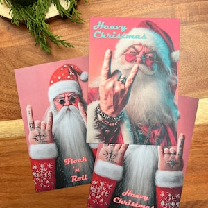 May include: Pink Christmas cards featuring a rock and roll Santa Claus with sunglasses, a white beard, and the text "Heavy Christmas" and "Flock 'n Roll". The cards have a festive design with red and white accents.