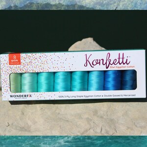 May include: A rectangular box containing eight spools of Konfetti 50wt Egyptian cotton thread in a gradient of green and blue shades. The white packaging features colorful confetti dots, the brand name Wonderfil, and product specifications.