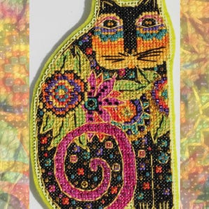 May include: A colorful, embroidered cat-shaped applique. The cat features a black face and body with intricate patterns in orange, green, purple, and pink. The applique is outlined in gold and has a light green border.