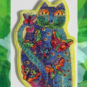 May include: A colorful, cross-stitched cat design with butterflies. The cat is primarily blue with green, orange, and gold accents. Butterflies in shades of pink, purple, and orange are scattered around the cat. The design is outlined in yellow.