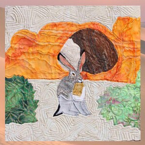 May include: A fabric art piece depicting a desert scene with a rabbit holding a small package. The artwork features a textured, quilted background with orange, brown, and green accents. The rabbit is gray and white, with long ears and a detailed face.